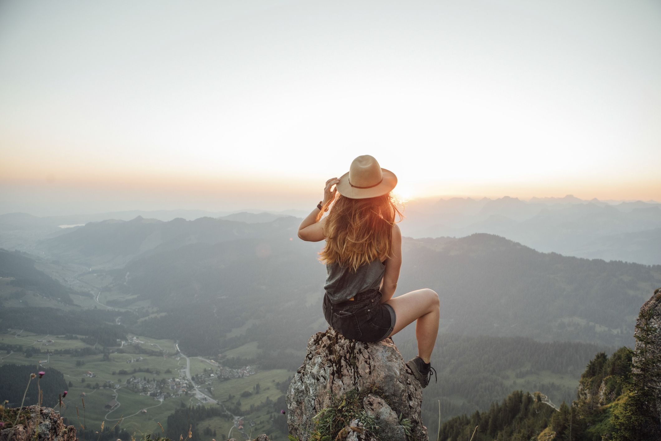 Junge Frau sitzt auf einem Felsen in den Bergen und blickt vertrauensvoll über das Panorama.