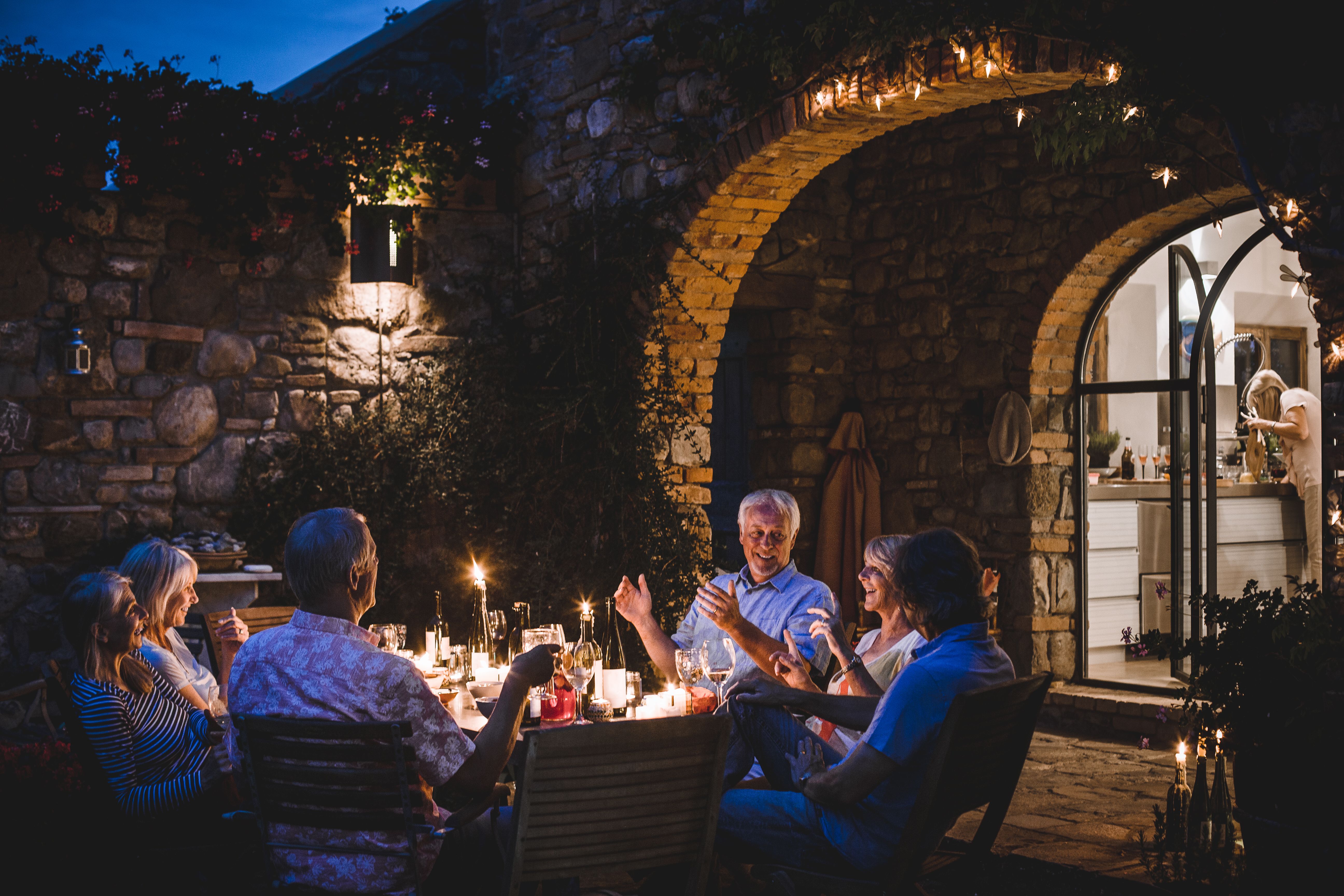 Gruppe lächelnder Freunde, die abends in einem Garten gemeinsam zu Abend essen und so einen Neuanfang, authentische Begegnungen und die Rückkehr ins soziale Leben nach einer Scheidung veranschaulichen.