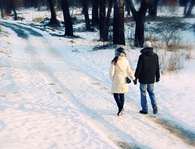 Online-Dating-Weihnachten: Ein Paar flaniert händchenhaltend durch den Schnee.